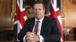 Sir Mark Spencer seated at a a desk, with Union Flags behind him.
