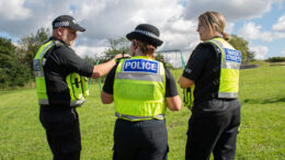 Two street wardens and a police officer talk in a field
