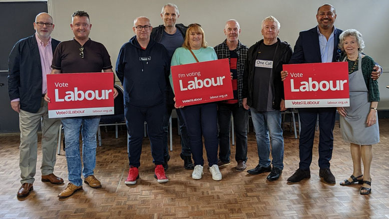 A small group of people hold Labour party placards in a community hall