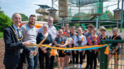 Old and young people standing in front of a ceremonial ribbon in front of an elevated play area