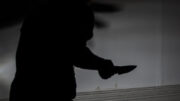 A silhouetted artistic image of a man holding a knife in a menacing way