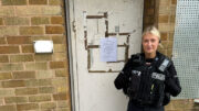 A police officer stands guard outside a boarded up house