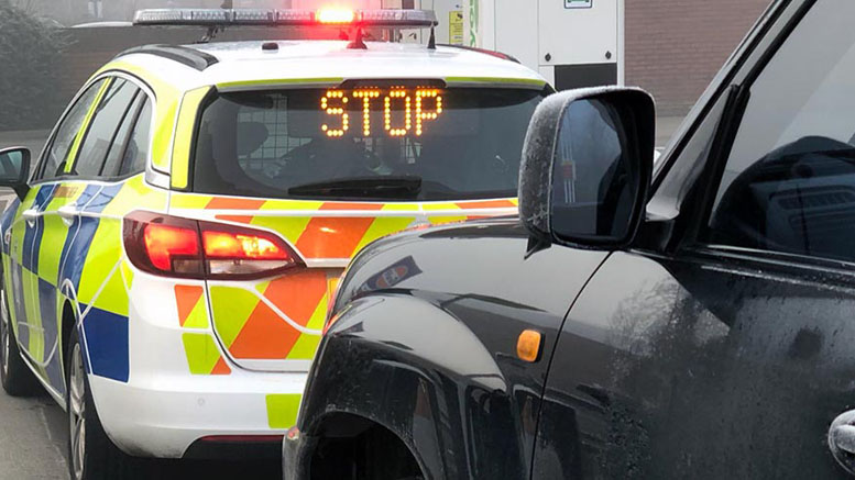 A marked police car displaying a "stop" LED sign in front of a car