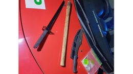 A machete, samurai sword, baseball bat and drugs placed on the bonnet of a red car