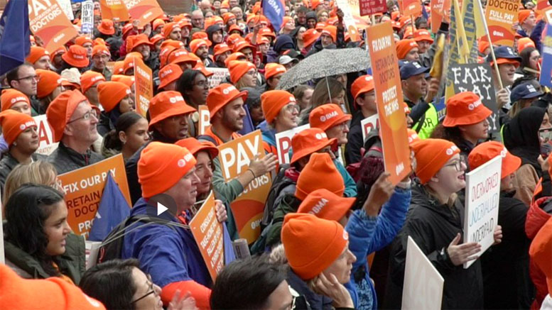 A crowd of doctors holding orange placards