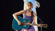 Taylor Swift on stage in a blue dress playing guitar