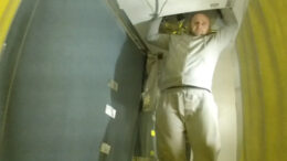 A tracksuit-wearing man lowers himself down from a loft hatch