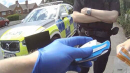 A police officer wearing blue gloves holds a knife while another holds an evidence bag.