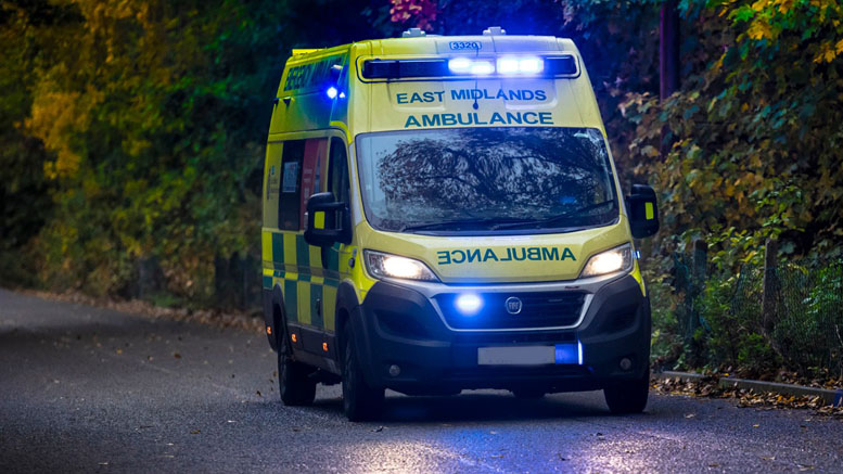 An ambulance travelling on a country road at dusk with blue lights on